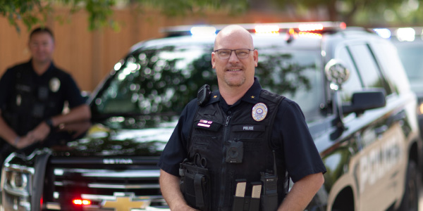 Police officer standing in fron of a police vehicle with lights flashing
